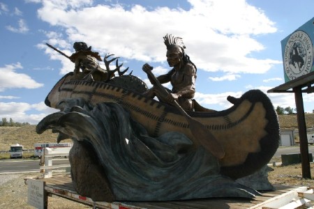  large bronze canoe with a hunter in the front, an indian in the back and an Elk pelt in the middle